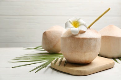 Young peeled coconuts with straw, palm leaf and flower on white wooden table. Space for text