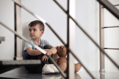 Sad little boy with toy sitting indoors