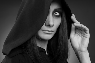 Mysterious witch with spooky eyes on dark background, closeup. Black and white effect