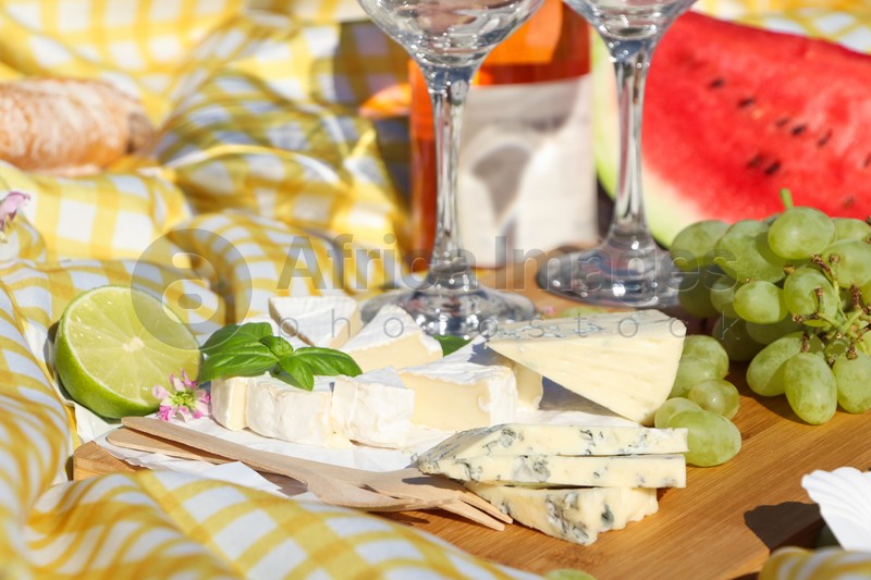 Delicious cheeses with basil and fruits on picnic blanket, closeup