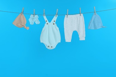 Different baby clothes drying on laundry line against light blue background