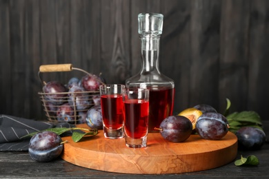 Photo of Delicious plum liquor and ripe fruits on black wooden table. Homemade strong alcoholic beverage