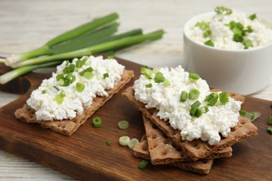 Photo of Crispy crackers with cottage cheese and green onion on white table, closeup