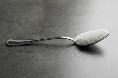 Spoon of white sugar on grey table