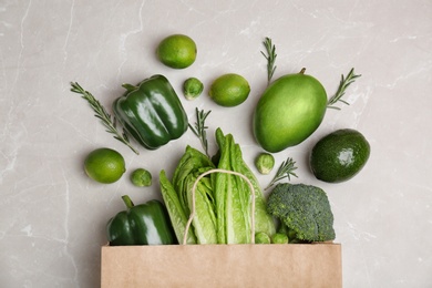 Paper package with green vegetables and fruits on grey background, top view