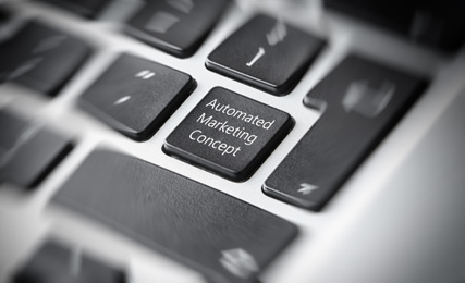 Modern laptop keyboard with text AUTOMATED MARKETING CONCEPT on button, closeup