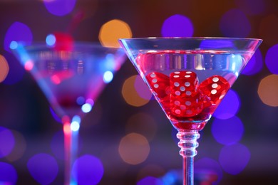 Cocktail with casino dice in glass against blurred lights, closeup. Space for text