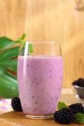Delicious blackberry smoothie in glass and berries on wooden board, closeup