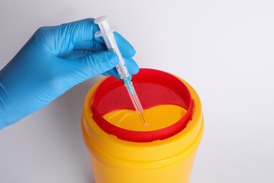 Doctor throwing used syringe into sharps container on white background, closeup