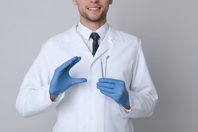 Dentist holding tools on light grey background, closeup
