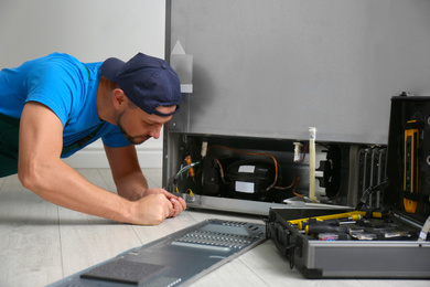 Photo of Male technician with screwdriver repairing refrigerator indoors