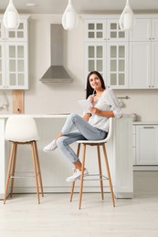 Beautiful young woman with notebook sitting on stool in kitchen