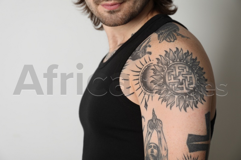 Young man with tattoos on body against white background, closeup