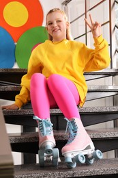 Photo of Cute indie girl with roller skates sitting on stairs indoors