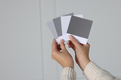 Photo of Woman with color sample cards choosing paint shade for wall indoors, closeup. Interior design