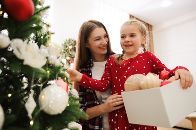 Happy mother with her cute daughter decorating Christmas tree together at home