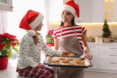 Mother giving her cute little daughter freshly baked Christmas cookies in kitchen