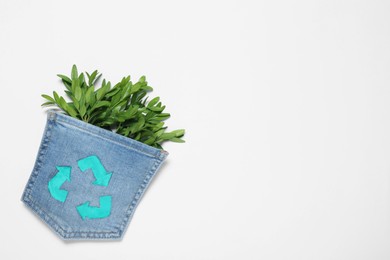 Twigs of green plant in jeans pocket with recycling symbol on white background, top view. Space for text