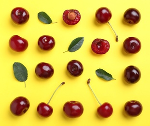 Sweet juicy cherries and leaves on yellow background, flat lay
