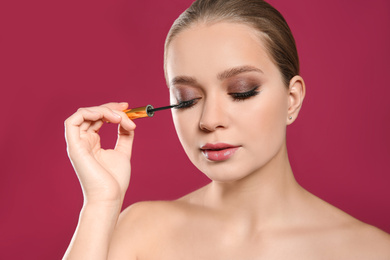 Beautiful woman applying eyeliner on pink background. Stylish makeup