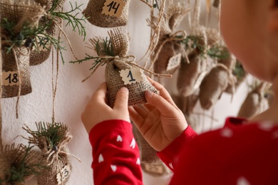 Photo of Little girl taking gift from New Year advent calendar indoors, closeup