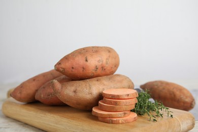 Wooden board with thyme and sweet potatoes on table