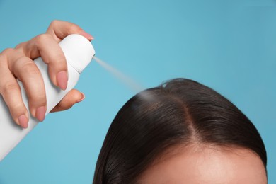 Young woman applying dry shampoo against light blue background, closeup