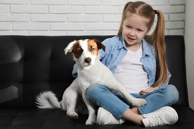 Cute little girl with her dog on sofa indoors. Childhood pet