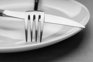 Photo of Plate with shiny silver cutlery on grey table, closeup