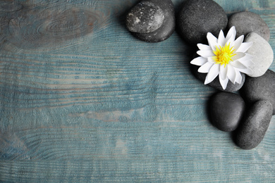 Stones with lotus flower and space for text on blue wooden background, flat lay. Zen lifestyle