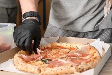 Professional chef adding prosciutto to Italian oven baked pizza in restaurant, closeup