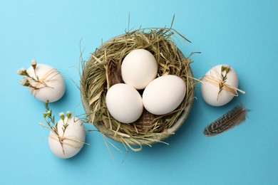 Photo of Nest with chicken eggs and natural decor on light blue background, flat lay. Happy Easter