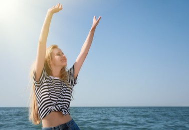 Beautiful young woman dancing near sea on sunny day in summer