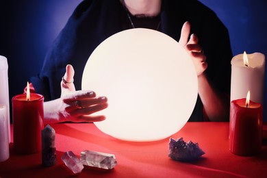 Soothsayer using glowing crystal ball to predict future  at table in darkness, closeup. Fortune telling