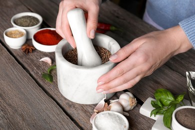 Photo of Woman grinding coriander at wooden table, closeup