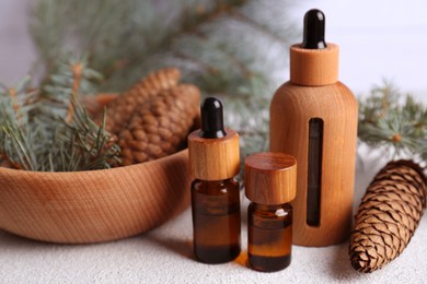 Bottles of aromatic essential oil, pine branches and cones on light grey table, closeup