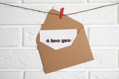 Envelope with I Love You card hanging on twine near white brick wall