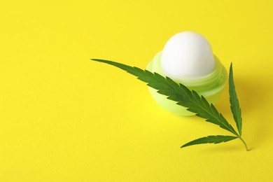 Hemp lip balm and green leaf on yellow background, space for text. Natural cosmetics