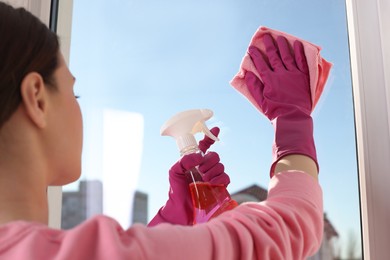Photo of Young woman cleaning window glass with rag and detergent at home