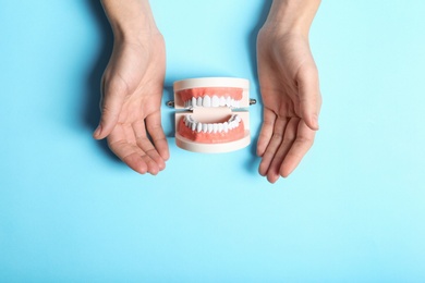 Woman holding hands near educational model of oral cavity with teeth on color background, top view. Space for text