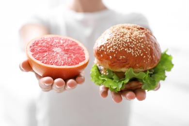 Photo of Concept of choice. Woman holding grapefruit and burger on white background, closeup