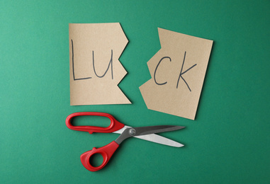 Cut paper with word LUCK and scissors on green background, flat lay