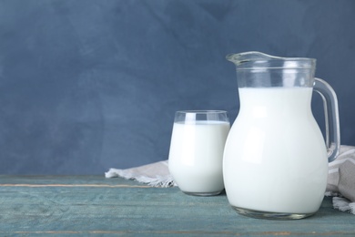 Jug and glass with fresh milk on wooden table against blue background. Space for text