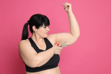 Photo of Obese woman with scissors on pink background, space for text. Weight loss surgery