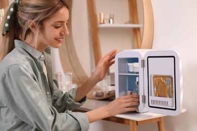 Woman taking cosmetic product from mini fridge indoors