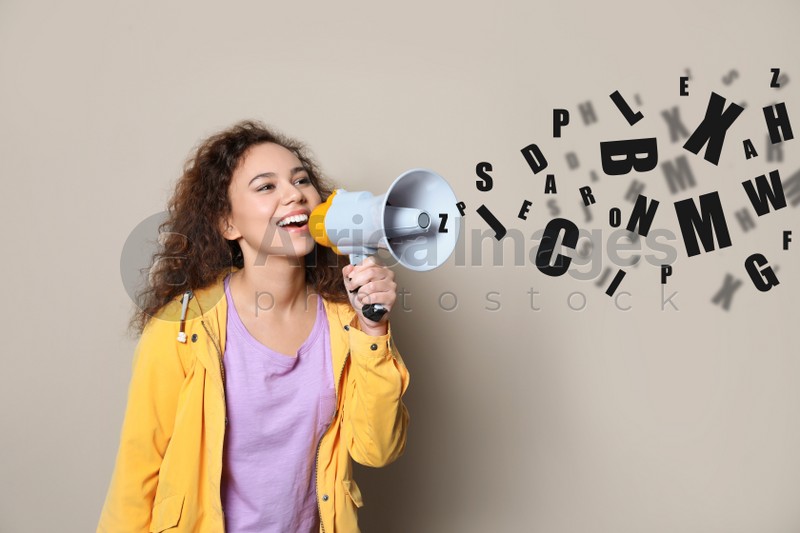 Young African-American woman with megaphone and letters on light background. Speech therapy concept