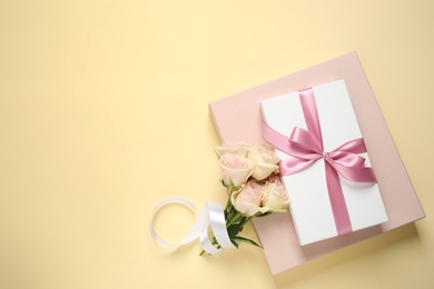 Elegant gift boxes and beautiful flowers on beige background, flat lay. Space for text