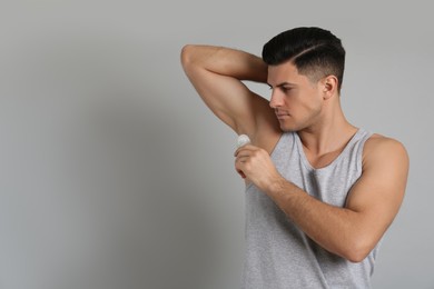 Handsome man applying deodorant to armpit on grey background, space for text