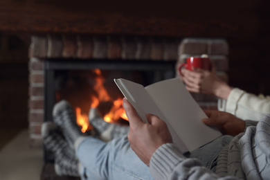 Man reading book and his girlfriend near burning fireplace at home, closeup