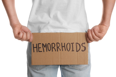 Photo of Man holding carton sign with word HEMORRHOIDS on white background, closeup